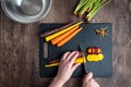 WomanÃ¢â¬â¢s hands cutting rainbow carrots on a black cutting board, stainless-steel bowl, wood table Royalty Free Stock Photo